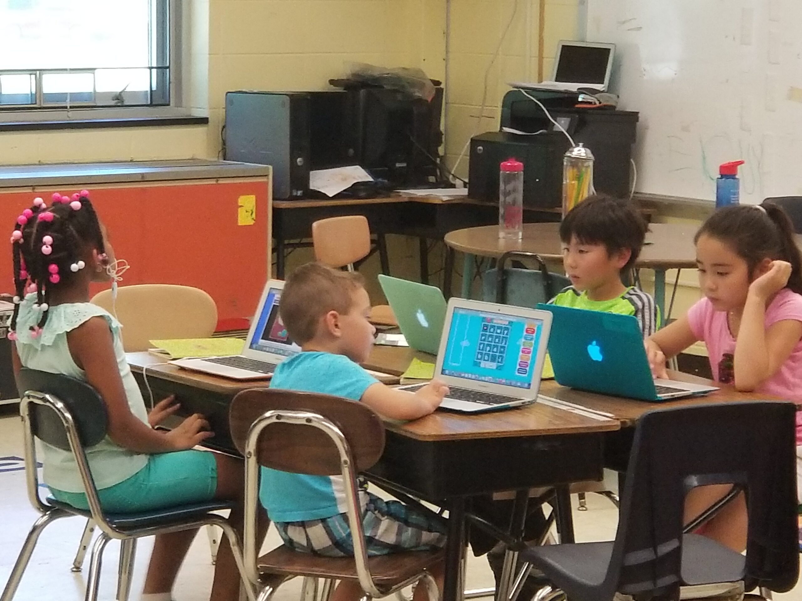 A group of children sitting at tables with laptops.